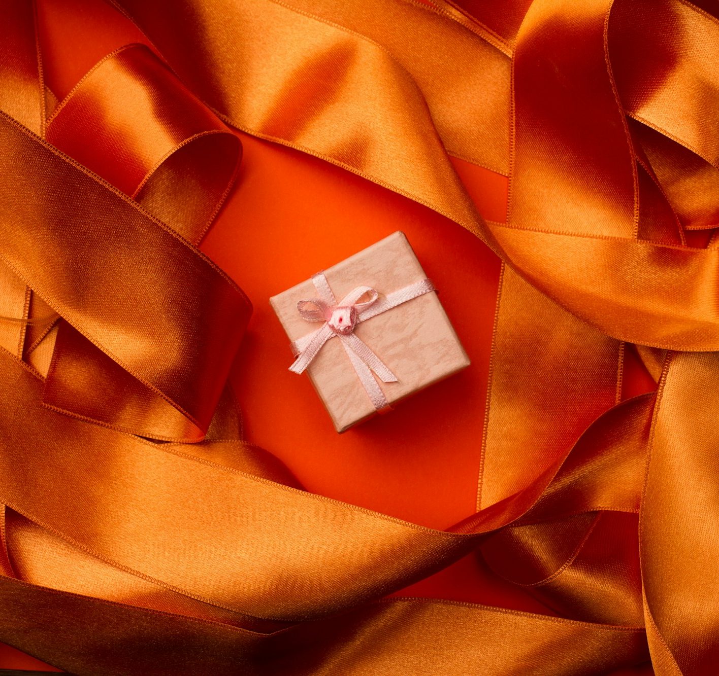 Top view of pink small gift box with ribbon on orange ribbon bac